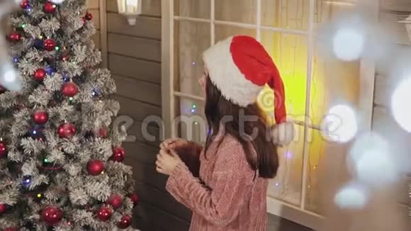 穿暖针织毛衣和圣诞帽的漂亮女孩装饰圣诞树视频的预览图