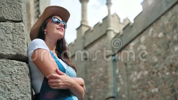 戴着太阳镜戴着帽子微笑着的女游客欣赏着中世纪高塔城堡视频的预览图