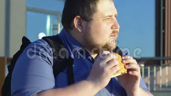 肥胖男学生在户外吃高热量汉堡快餐和超重视频的预览图