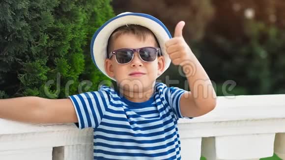 戴帽子戴太阳镜的可爱的小男孩表现出冷静的姿态大拇指在户外玩得开心视频的预览图
