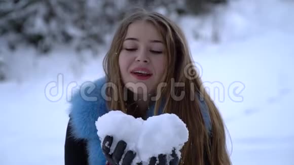 年轻漂亮的女孩走在白雪皑皑的冬林里她既快乐又开朗女孩用手掌吹雪视频的预览图