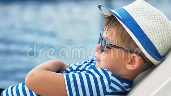 戴墨镜和帽子的欧洲男孩躺在甲板椅上交叉双臂竖起拇指放松视频的预览图