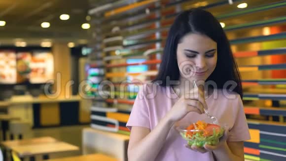 快乐的白种人女士吃着新鲜的素食沙拉站在快餐店里视频的预览图
