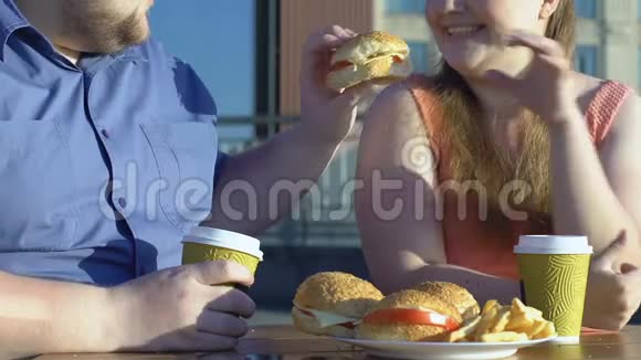 大胖男人在户外咖啡馆给女友吃汉堡吃垃圾食品视频的预览图