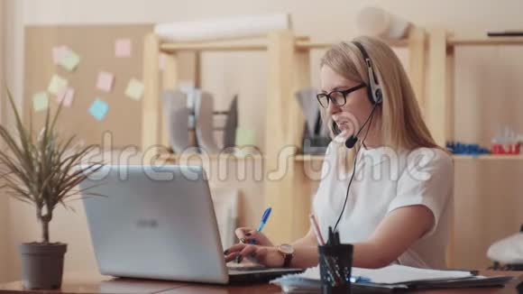 一个漂亮的年轻女孩在电话中心做接线员在耳机上讲话在电脑上工作视频的预览图
