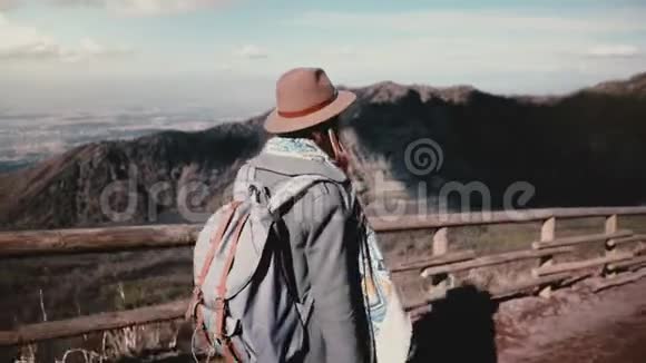 女游客戴着帽子背着背包走在山路上用木栅栏欣赏着令人惊叹的景色视频的预览图