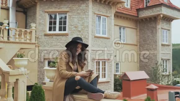 一位卷发的美女坐在一座古老的石头城堡的阳台栏杆上给她的朋友写短信用一个视频的预览图