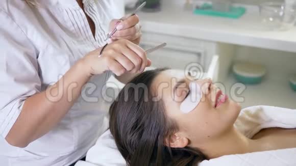 美容院的师傅和客户专业造型师用专用胶水和两把镊子拉长女睫毛视频的预览图