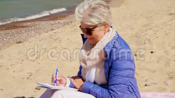 一位年长的女士在夏日海滩上写笔记本视频的预览图
