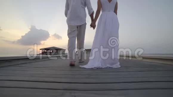 蜜月旅行在热带地区新娘穿着白色礼服和新郎一起走在木制码头上在豪华的平房里视频的预览图