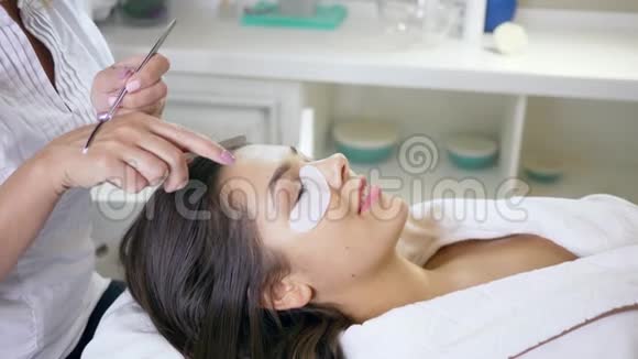 美容院的工作人员用镊子将睫毛粘在睫毛上女工在睫毛过程中用眼贴视频的预览图