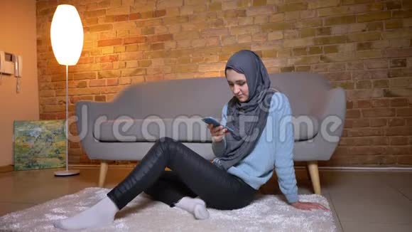 年轻迷人的穆斯林女性在舒适的家中坐在地板上发短信时的特写镜头视频的预览图