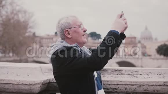 喜笑颜开的欧洲资深男士在意大利罗马的智能手机拍照退休度假旅行慢动作视频的预览图