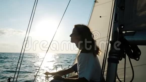 快乐的年轻女子穿着礼服坐在桅杆旁的甲板上日落时扬帆远航视频的预览图