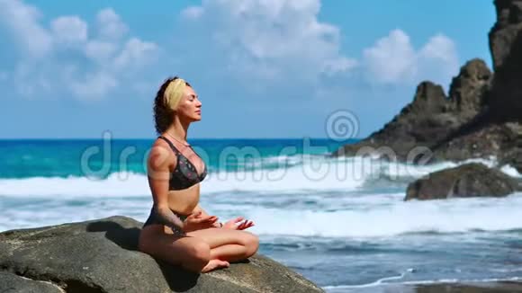 日落时瑜伽练习雍女坐在石上莲姿慢悠悠地在美丽的晨滩上沉思视频的预览图