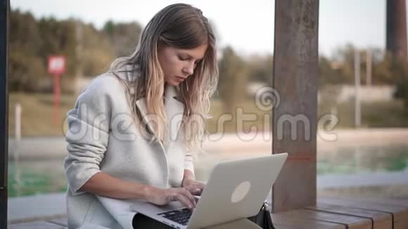 穿着白大褂的严肃女人坐在池塘边的笔记本上打字视频的预览图