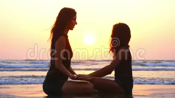 日落时分妈妈和女儿一起坐在沙滩上手牵手视频的预览图