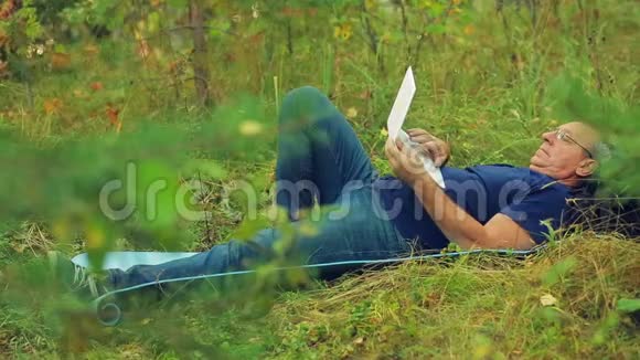 一个男人躺在公园的草地上用笔记本电脑工作视频的预览图