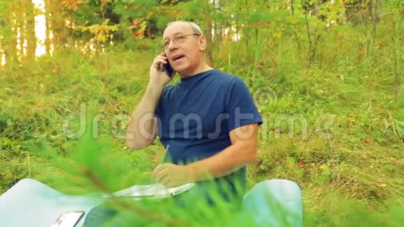 森林里的一个人在笔记本上工作在手机上说话视频的预览图