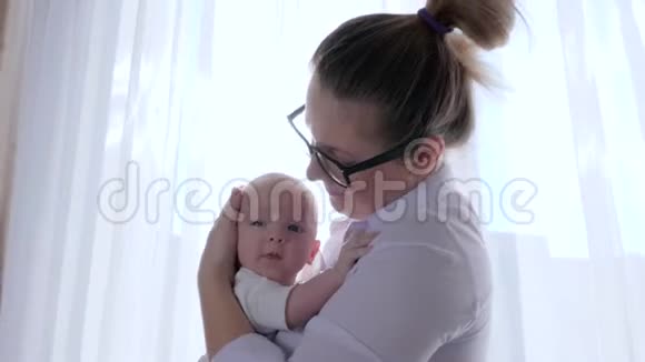 母婴关系年轻的妈妈在靠近窗户的自然光线下把婴儿抱在房间里视频的预览图