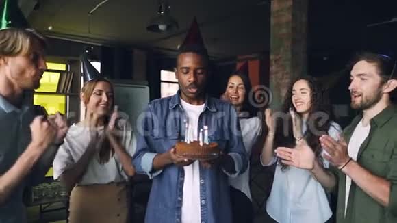 兴奋的非洲裔美国人在生日蛋糕上吹蜡烛在他的团队中大笑视频的预览图