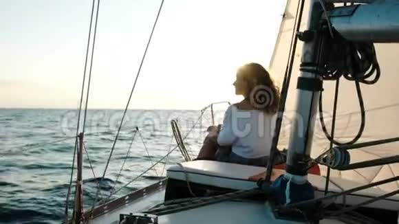 年轻女孩穿着裙子坐在桅杆附近的帆船甲板上视频的预览图