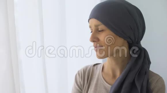戴头巾的快乐女人看着窗外癌症治疗后恢复视频的预览图