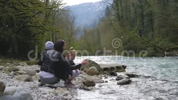 妈妈带着两个蹒跚学步的孩子在河边户外玩耍视频的预览图