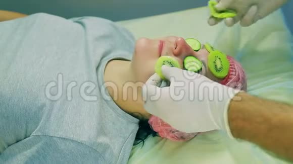 化妆师的男人的手在一个女性的脸上贴上一个来自猕猴桃和黄瓜片的面具视频的预览图