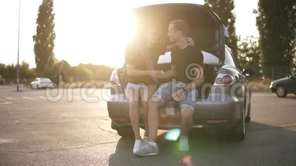 微笑的夫妇坐在停车场上的现代银色汽车的后备箱里聊天在一起玩得很开心夏季视频的预览图