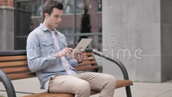 休闲青年坐在户外为平板电脑的成功欢呼视频的预览图