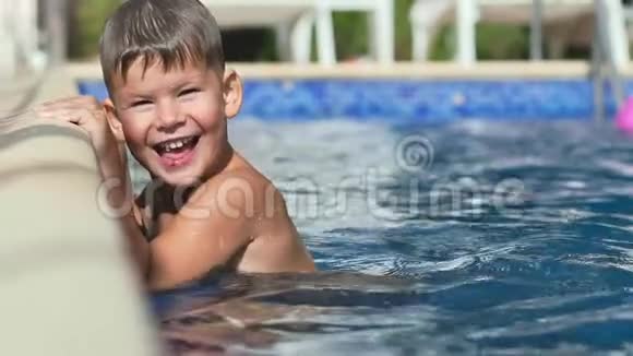 快乐微笑的小男孩双手斜靠在游泳池边享受着快乐的慢动作视频的预览图