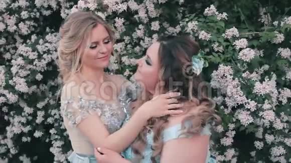 两个姐姐穿着蓝色的llight豪华的奇妙连衣裙在花园里靠近白花女人轻轻地纠正视频的预览图