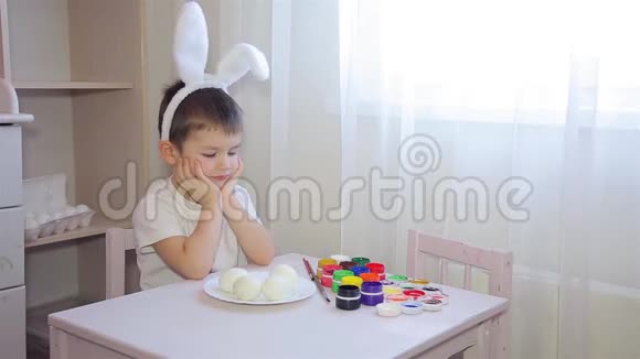 一个打扮成兔子的男孩画一个复活节彩蛋视频的预览图