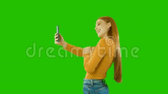 年轻女孩留着长发做着不同的姿势对着相机手机自拍绿色背景微笑视频的预览图
