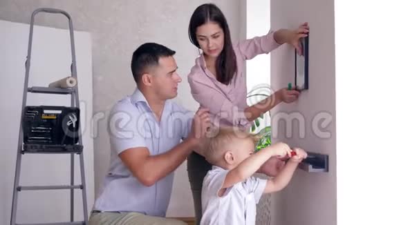 友好的家庭做修理小儿子帮助父母在新公寓的墙上系好架子视频的预览图