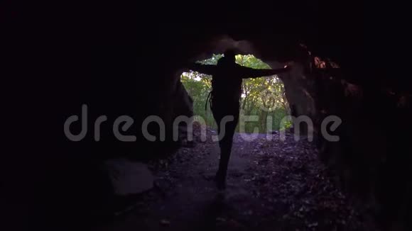 一个背着背包的游客从黑暗的山洞里跑出来举起手来慢吞吞的视频的预览图