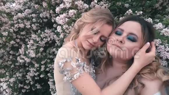 两个穿着蓝色llight豪华奇装异服的姐妹正拥抱在白花旁的花园里1名妇女视频的预览图
