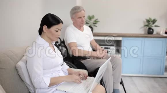 在当地的一家医院一名护士在轮椅上照看一个灰发男子视频的预览图