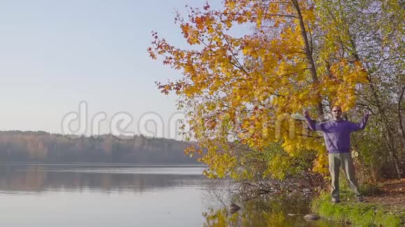 一个穿着蓝色毛衣的男人挥动着他的手在秋天的森林里的湖面上展示了成功视频的预览图