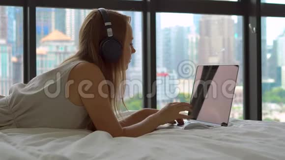 年轻的女性自由职业者在她的笔记本电脑上工作当她听到电话时她会摘下耳机躺在床上视频的预览图