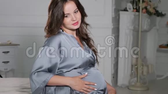 怀孕休息人和期望的概念快乐的孕妇坐在床上触摸她的腹部在家里视频的预览图