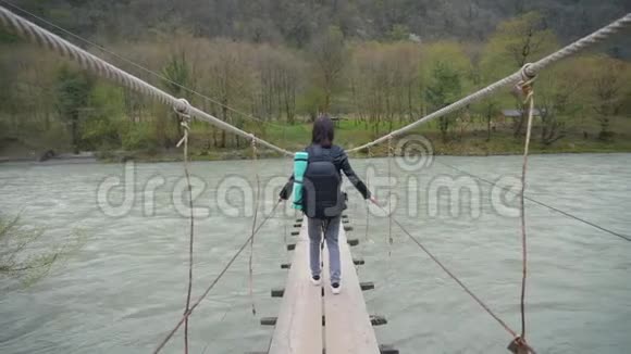 女孩旅行者带着背包在悬索桥上过河木头渡船过河女徒步旅行者视频的预览图