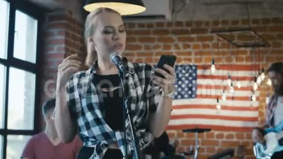 带着智能手机的女孩在乐队里唱歌视频的预览图