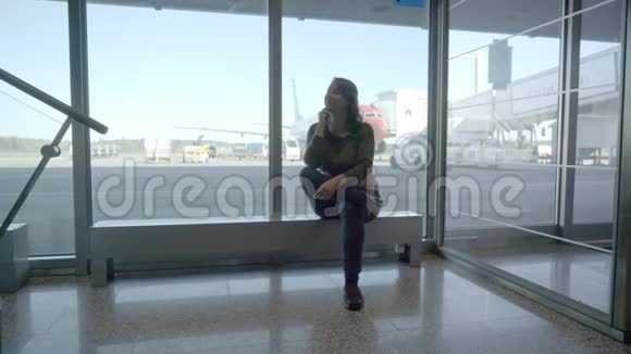 年轻的女游客在机场透过窗户看飞机视频的预览图
