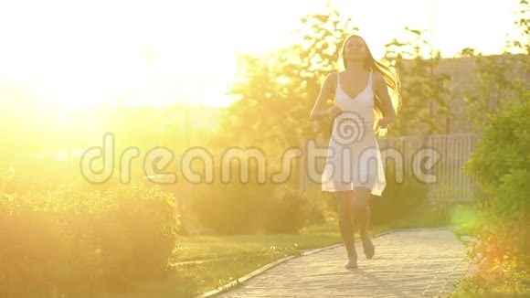 美丽的女孩在绿色公园的夏日里在夕阳下奔跑着玩自由健康幸福的理念快乐视频的预览图