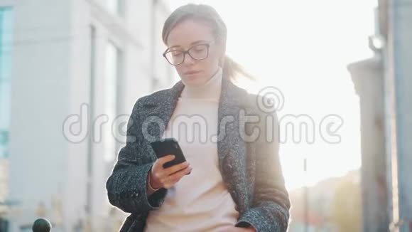 一个手里拿着智能手机的年轻女人的肖像女孩在户外使用手机视频的预览图