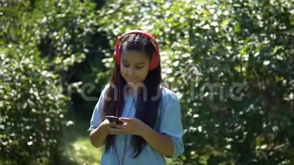一个长发迷人的女孩走过公园用耳机听音乐慢吞吞的高清高清视频的预览图