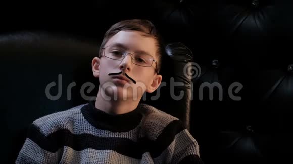 一个戴着眼镜和瘦小胡子的年轻人坐在一张黑色的皮椅上陷入了沉思像作家或学生这样聪明的人视频的预览图