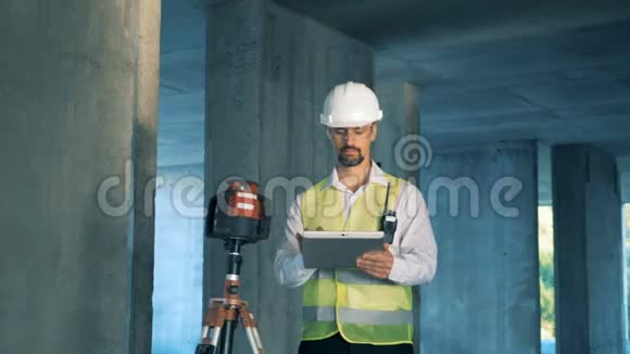 男建筑检查员站在陆地测量装置附近正在制作他的平板电脑视频的预览图